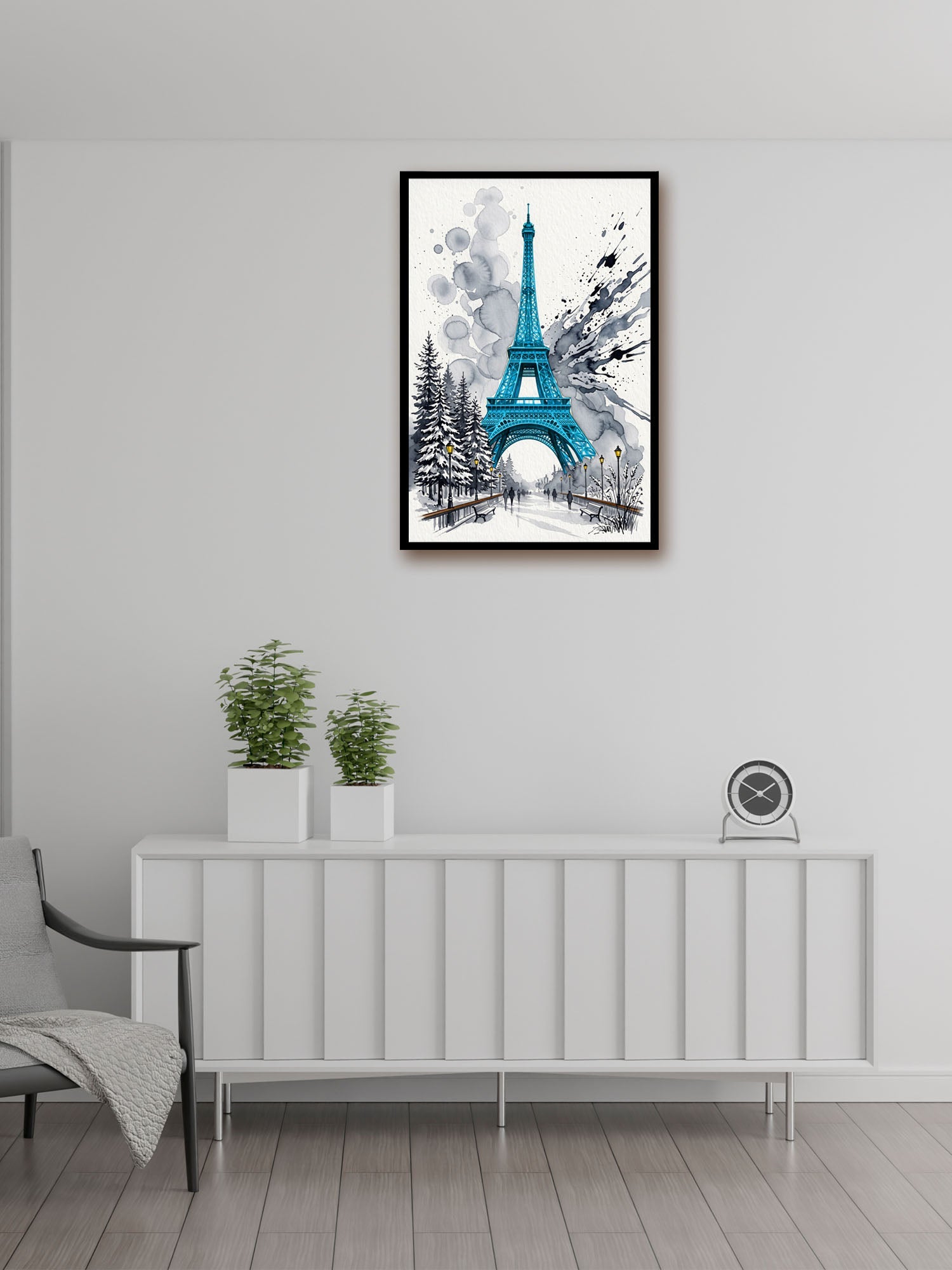 A framed vertical art print of the Eiffel Tower in a winter scene, featuring a vibrant teal blue tower and snowy trees, displayed on a light gray wall above a white sideboard in a modern room setting.