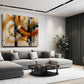 A modern living room featuring a large abstract canvas wall art print with gold, orange, black, and white brushstrokes, hung above a gray sectional sofa.
