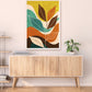 Colorful abstract leaf art on a wall above a wooden cabinet.