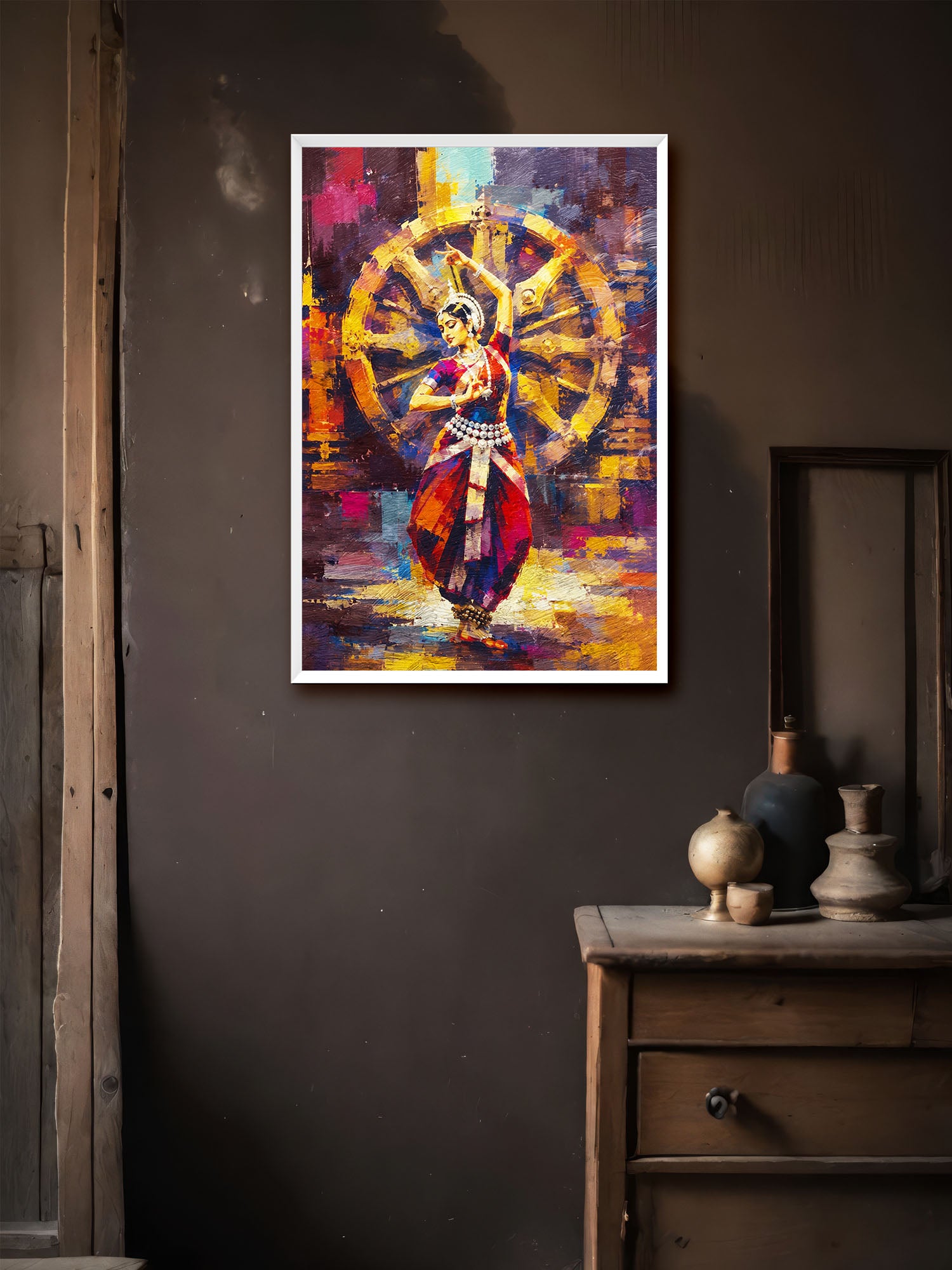 A framed colorful wall art print depicting a dancer in front of a large wheel, displayed on a dark wall above a wooden cabinet with decorative vases.