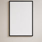 A minimalist black picture frame with a blank white mat, mounted on a neutral beige wall.