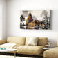 A rectangular canvas wall art print depicting a Brihadeeswara temple gopuram under a cloudy sky, displayed on a white wall above a beige fabric sofa in a modern living room setting.