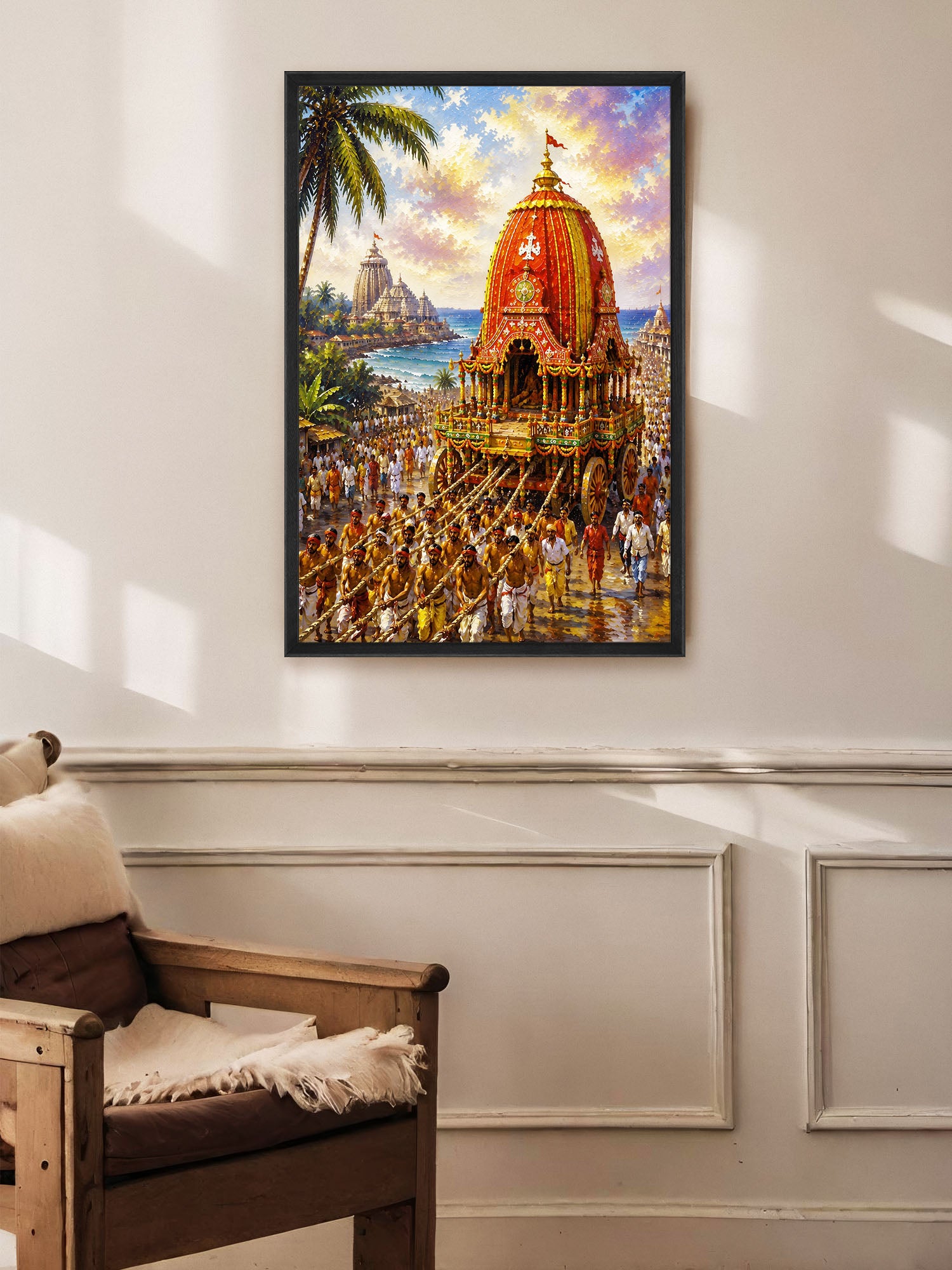 A framed colorful painting of a traditional Indian temple procession with a decorated chariot, displayed on a white paneled wall above a wooden armchair.
