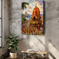 A vertical canvas print of a Hindu temple festival, depicting a decorated palanquin carrying devotees toward a temple, displayed on a textured gray concrete wall in a modern room setting with a potted plant and a wooden bench.
