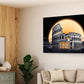 A rectangular wall art print showing the Colosseum under a large glowing orange sun, displayed on a beige wall in a modern living room with a sofa, wood-paneled wall, and plants.
