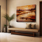 An abstract landscape canvas print with warm orange, brown, and gold tones, displayed on a beige wall above a wooden bench in a modern, sunlit entryway.