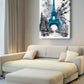 A vertical canvas wall art print featuring a bright blue Eiffel Tower in a snowy Paris street, styled in a modern living room above a cream-colored sectional sofa.