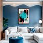 A modern living room featuring a white sectional sofa with decorative pillows, a round blue velvet ottoman, and a blue accent wall with a wavy pattern. A framed abstract geometric art print hangs on the wall above the sofa.