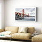 A framed wall art print of the Golden Gate Bridge hanging above a beige sofa in a bright, modern living room.
