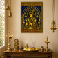 A framed gold and blue wall art print depicting a Krisha deity, displayed in a warm, traditional room setting above a wooden altar with brass lamps and decorative items.