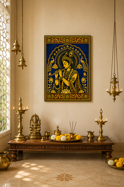 A framed gold and blue wall art print depicting a Krisha deity, displayed in a warm, traditional room setting above a wooden altar with brass lamps and decorative items.