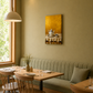 A warm, modern dining nook with a light wood table, wooden spindle-back chairs, a green pleated banquette, and a textured olive-green wall featuring a gold-toned still life painting.