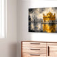 A rectangular canvas wall art print depicting the Golden Temple in Amritsar, rendered in a textured golden-yellow and gray painting with reflections in water, displayed on a white wall above a wooden dresser.