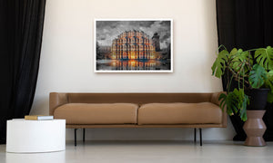 A framed art print depicting a grand illuminated palace with warm golden light reflections on water, displayed on a beige wall above a brown leather sofa in a modern living room setting.