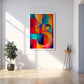 A colorful abstract wall art print with bold geometric shapes in red, blue, yellow, orange, and green, displayed in a white frame on a light gray wall in a modern room setting with a plant and a small side table.