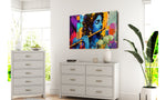 Colourful krishna abstract painting of a musical instrument on a wall above white dressers with a plant in the foreground.