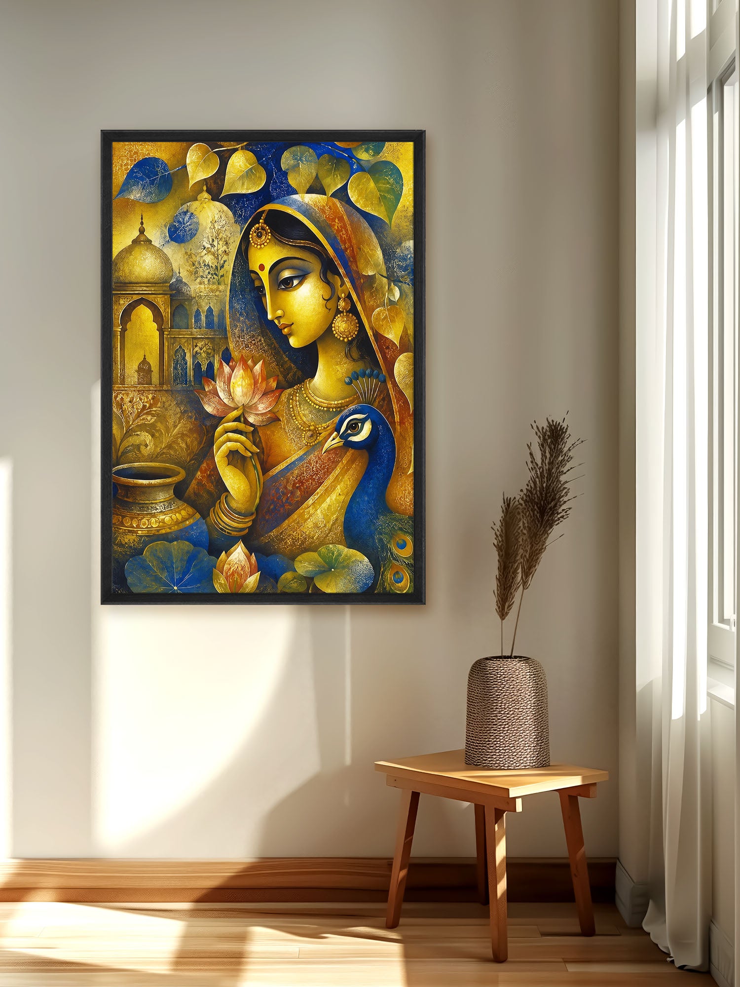 A framed vertical art print depicting a stylized woman in gold and blue attire with a peacock and lotus flower, displayed on a beige wall in a sunlit room above a small wooden stool with a vase.