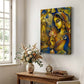 A vertical canvas wall art print featuring a stylized golden-skinned goddess with a peacock, displayed on a white wall above a wooden console table with a vase of flowers and a small clock.