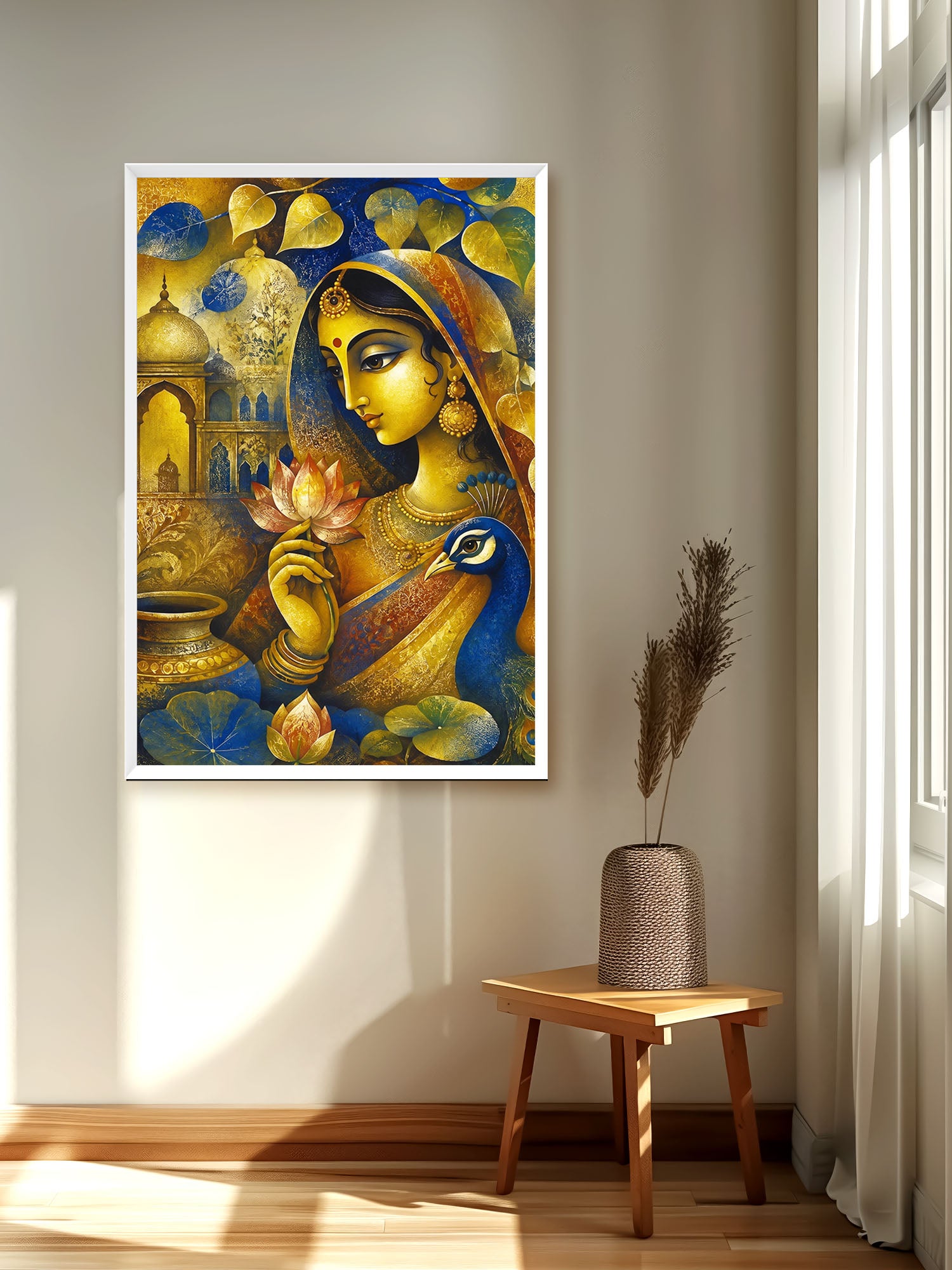A framed vertical art print featuring a stylized golden woman with a peacock and lotus motifs, displayed on a beige wall in a sunlit room above a small wooden stool with a vase.