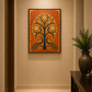 A framed vertical canvas art print featuring a stylized tree of life with peacocks, displayed on a beige wall in a hallway with a rug and a dark wooden console table with a potted plant.