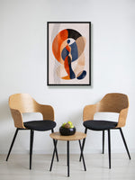 A framed abstract art print hangs on a white wall above two modern wooden chairs with black seats and a small round wooden side table in between.