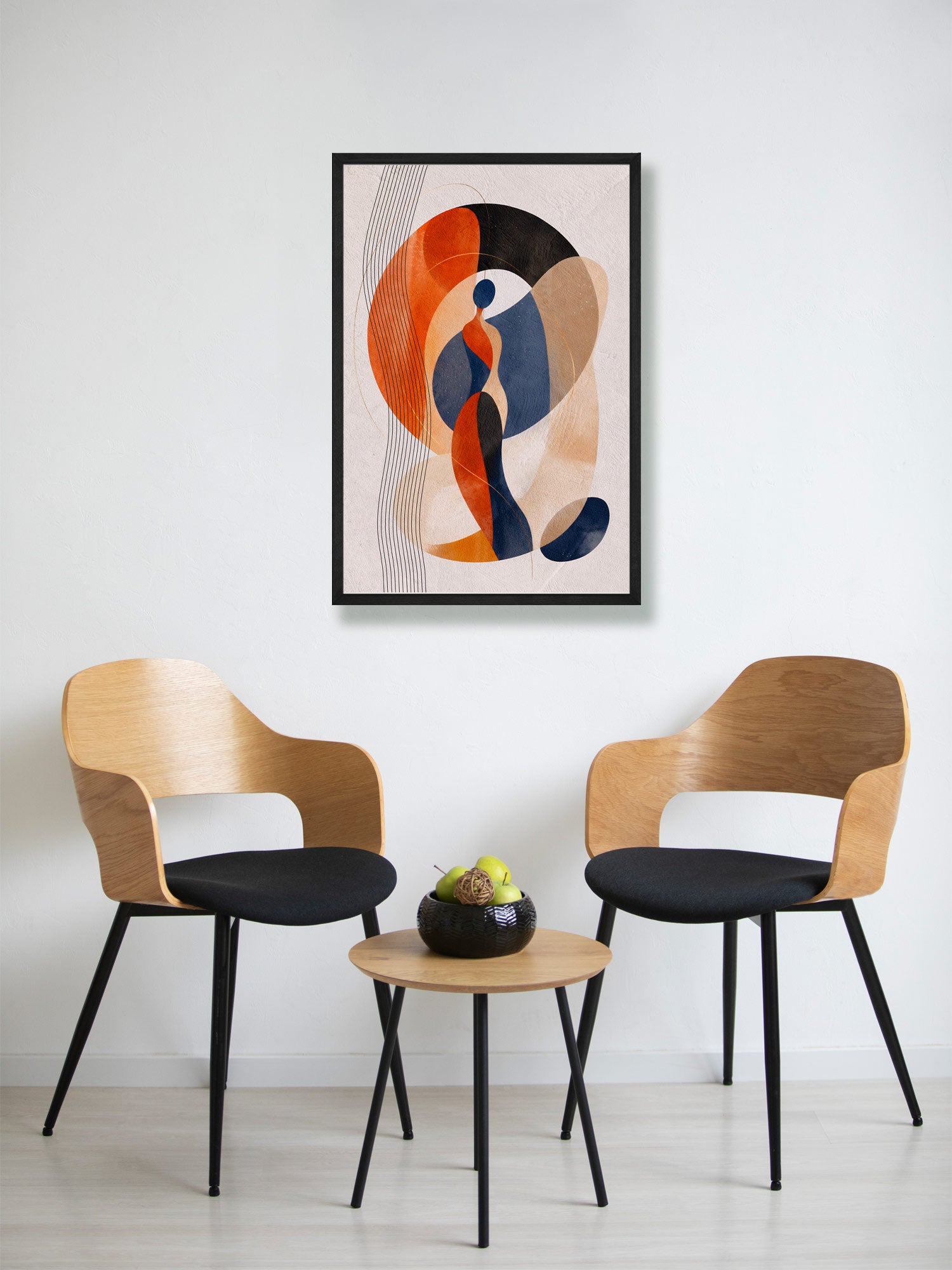A framed abstract art print hangs on a white wall above two modern wooden chairs with black seats and a small round wooden side table in between.