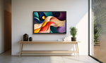 A framed abstract art print with flowing waves of blue, purple, orange, yellow, and red hangs on a white wall above a light wood console table in a modern interior setting.