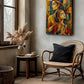 A colorful framed wall art print depicting two stylized figures hangs on a textured plaster wall in a rustic living room setting with a rattan chair, side table, and pampas grass.