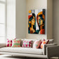 A colorful abstract canvas wall art print depicting two stylized faces, displayed in a modern living room setting above a light gray sofa with patterned pillows.