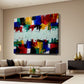 A large abstract canvas wall art print with vibrant multicolor brushstrokes is displayed in a modern living room setting above a beige sectional sofa.