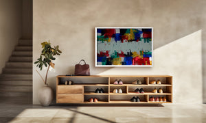 A colorful abstract canvas print with a white frame hangs on a beige wall above a wooden shoe cabinet in a modern, sunlit entryway.