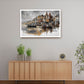 A framed art print depicting a scenic harbor with boats and buildings, displayed on a light gray wall above a wooden sideboard in a modern room setting.