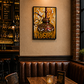 A framed art print depicting a hookah set against a golden background, displayed on a beige wall in a cozy, dimly lit pub with brown leather booths and a wooden table.