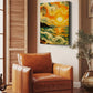 A square canvas wall art print featuring a swirling, impressionistic sunset landscape in yellow, orange, green, and cream tones, displayed on a beige wall above a brown leather armchair in a styled room.